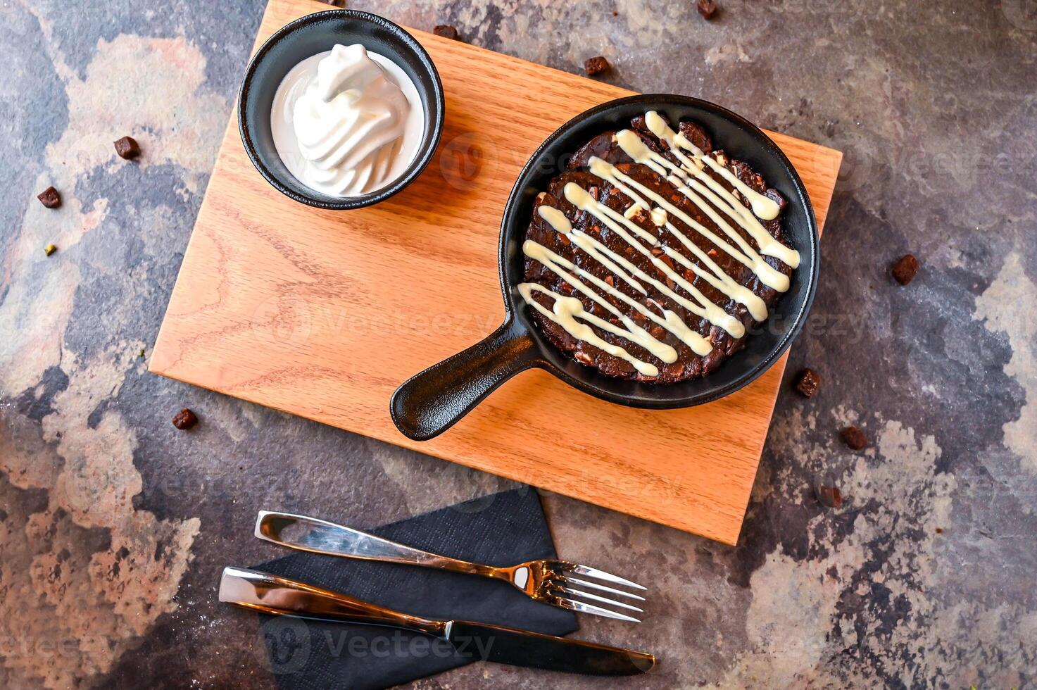 Double chocolate Chip Cookie dough with white chocolate, whipped cream, knife and fork served in dish isolated on dark background closeup top view of cafe baked dessert food photo