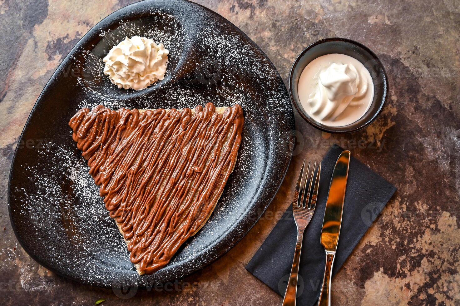 Nutella Crepe Hot Chocolate with whipped cream, knife and fork served in dish isolated on dark background closeup top view of cafe baked dessert food photo