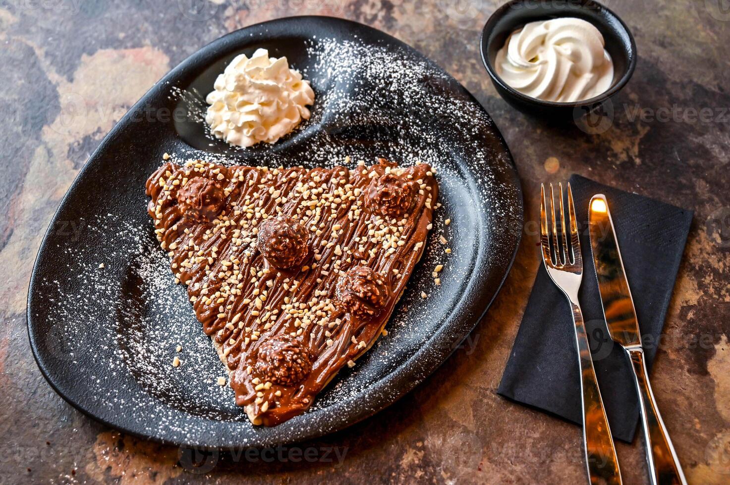 ferrero rocher crepe con caliente chocolate, azotado crema, cuchillo y tenedor servido en plato aislado en oscuro antecedentes de cerca parte superior ver de café horneado postre comida foto