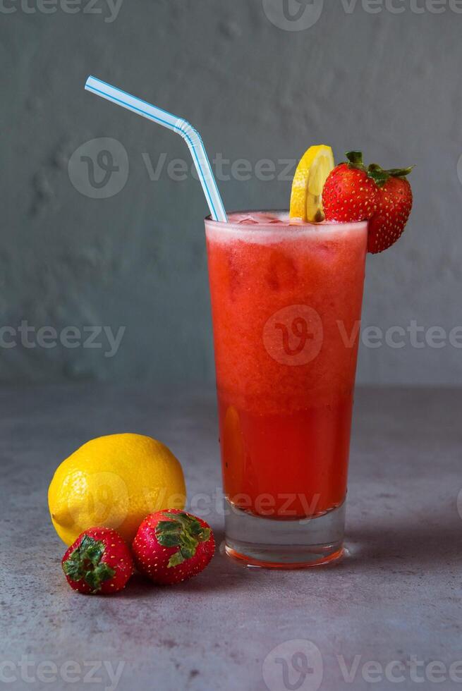 sano fresa limonada Fresco jugo servido en vaso con fresa y limón rebanada Paja lado ver en gris antecedentes foto