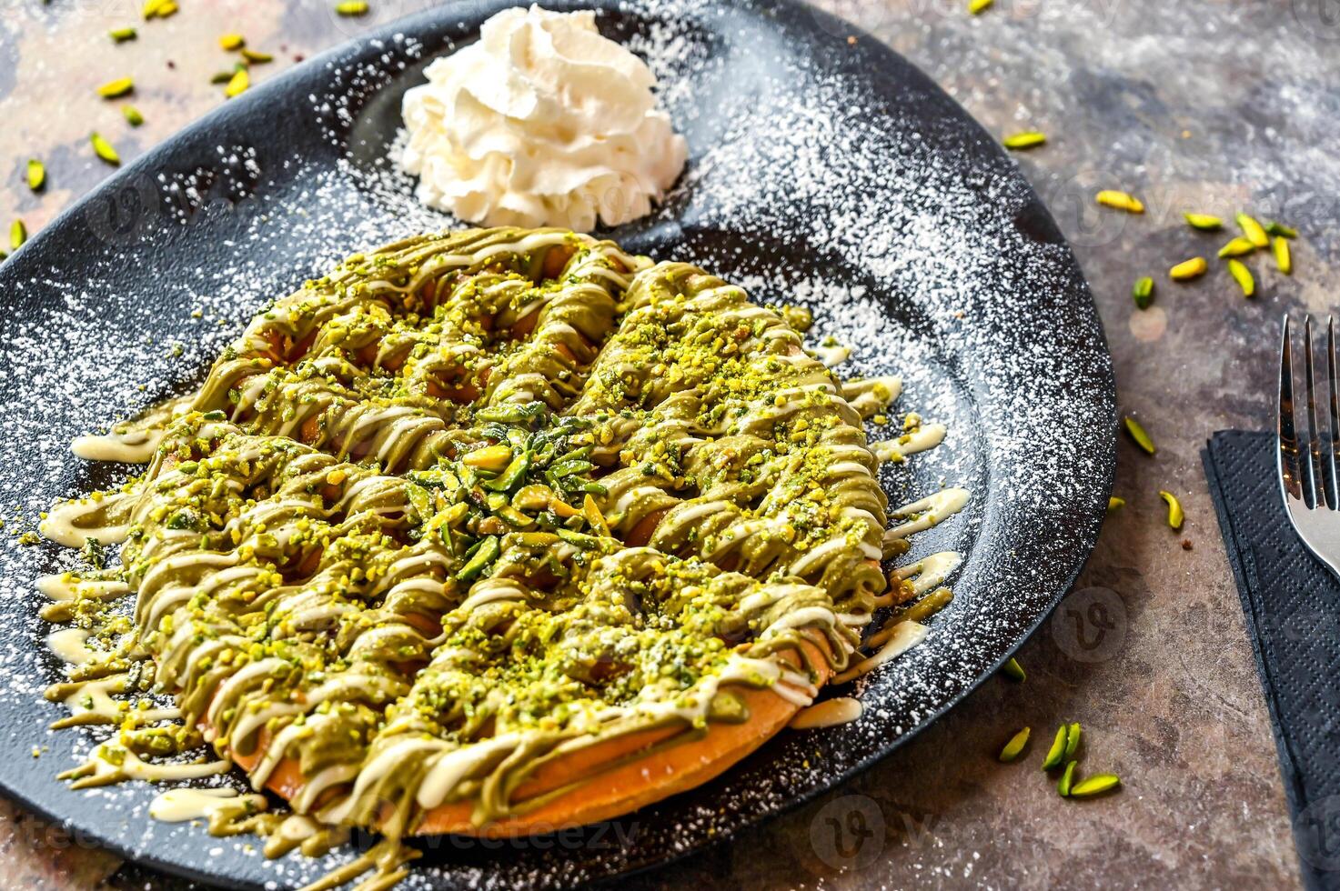 Pistachio Waffle with chocolate, whipped cream, knife and fork served in dish isolated on dark background top view cafe dessert food photo