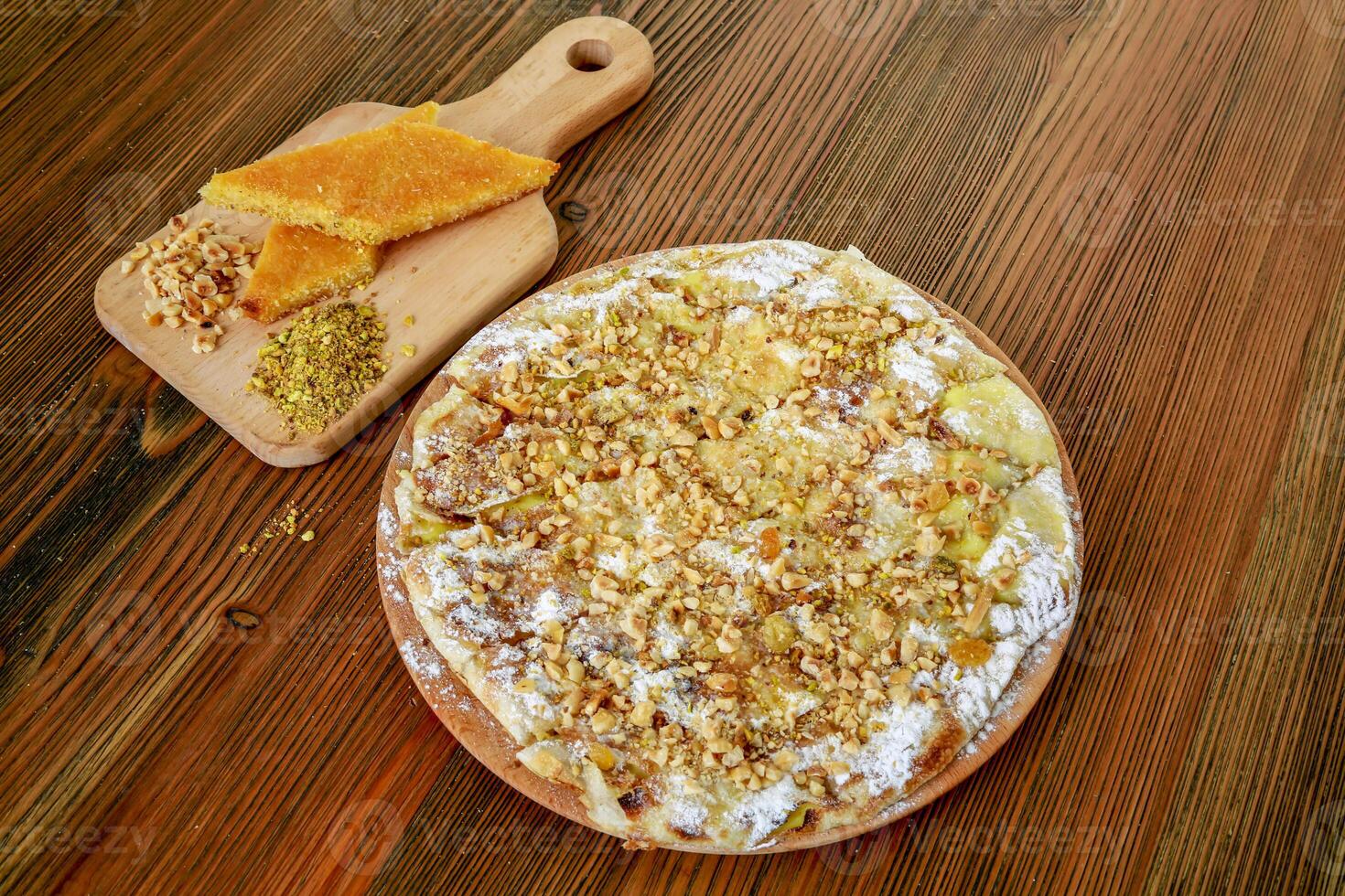 Basbousa nuts pie with pistachio and walnut served in wooden board isolated on table side view of arabic food photo