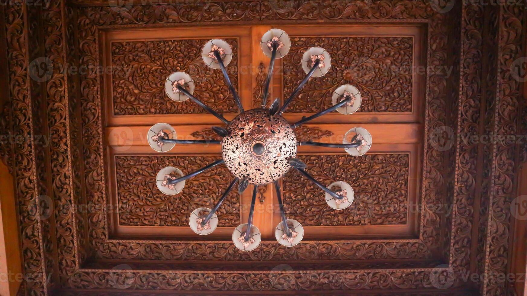 Beautiful retro chandelier on wood carving ceiling in traditional javanese house interior. photo