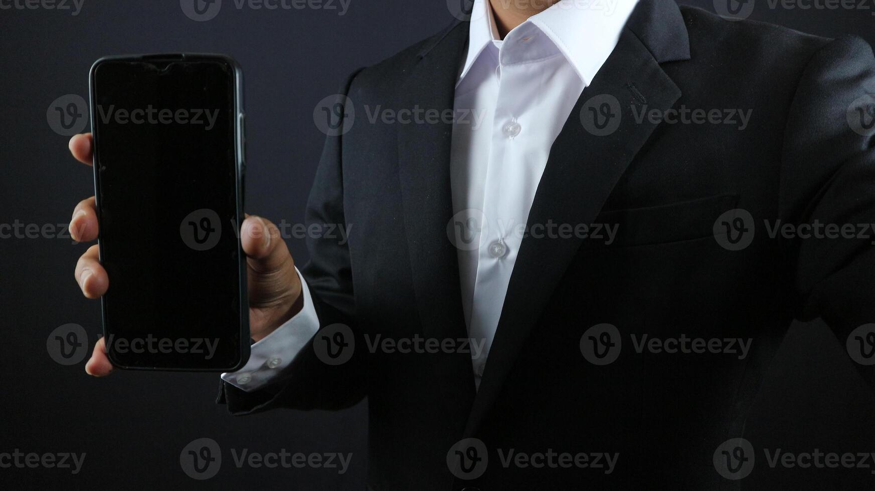 Businessman in a black suit showing smartphone with vertical blank white screen.Horizontal mockup photo
