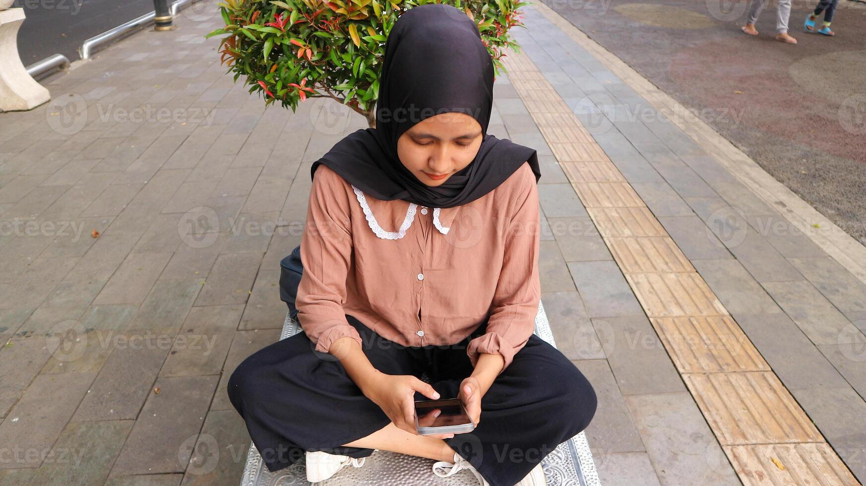 portrait of Muslim woman using mobile phone reading message at city park. Enjoying, relaxing weekend photo