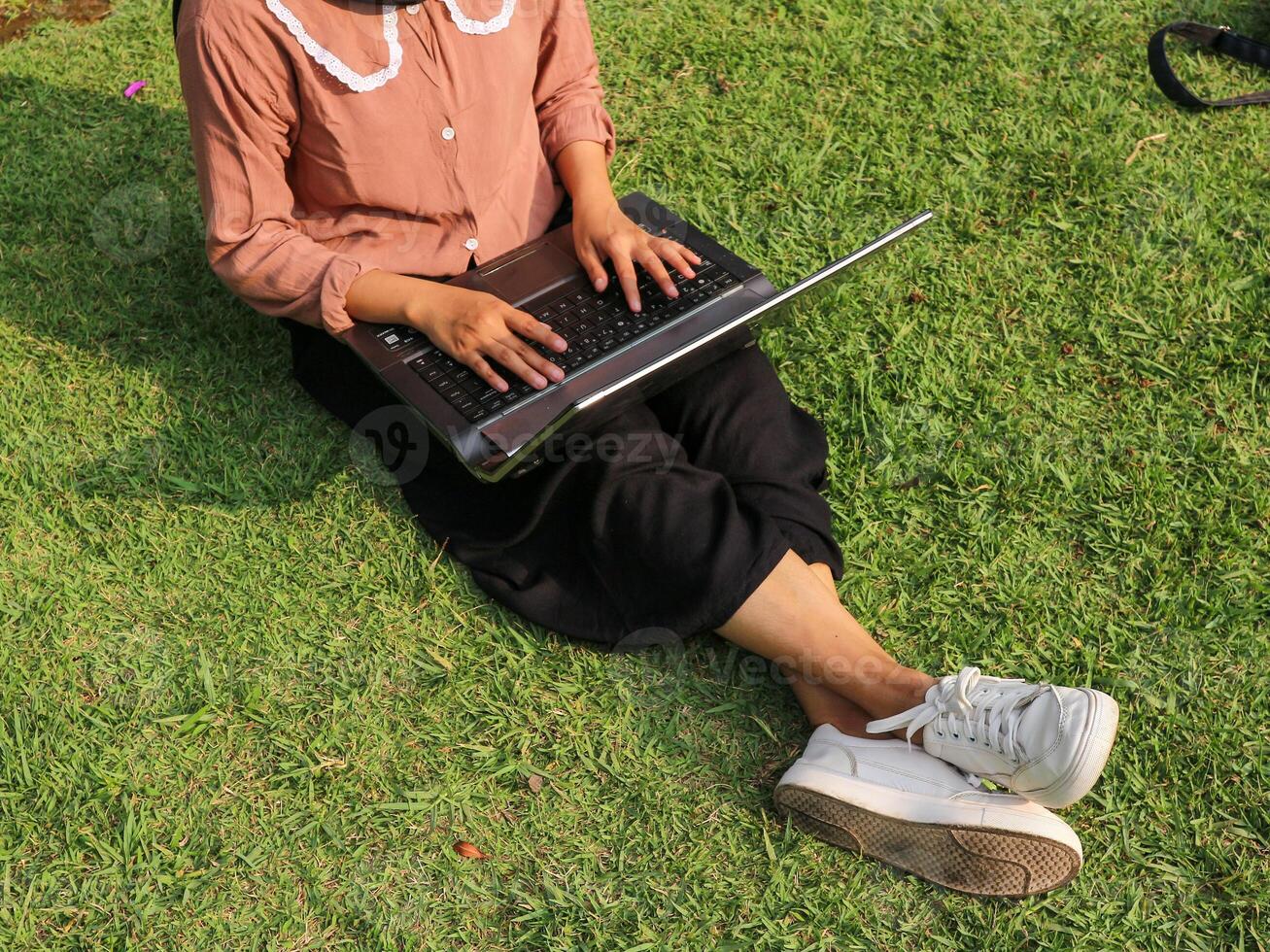 Top view of woman sitting in park on the green grass with laptop, hands on keyboard. photo