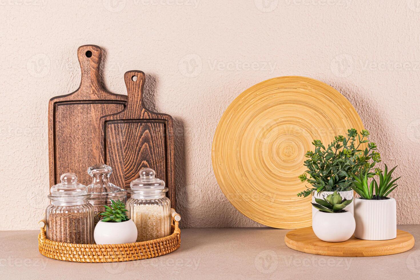 Set of glass jars with spices on a round wicker tray on a stone countertop. Potted houseplants. Kitchen background. Front view. photo