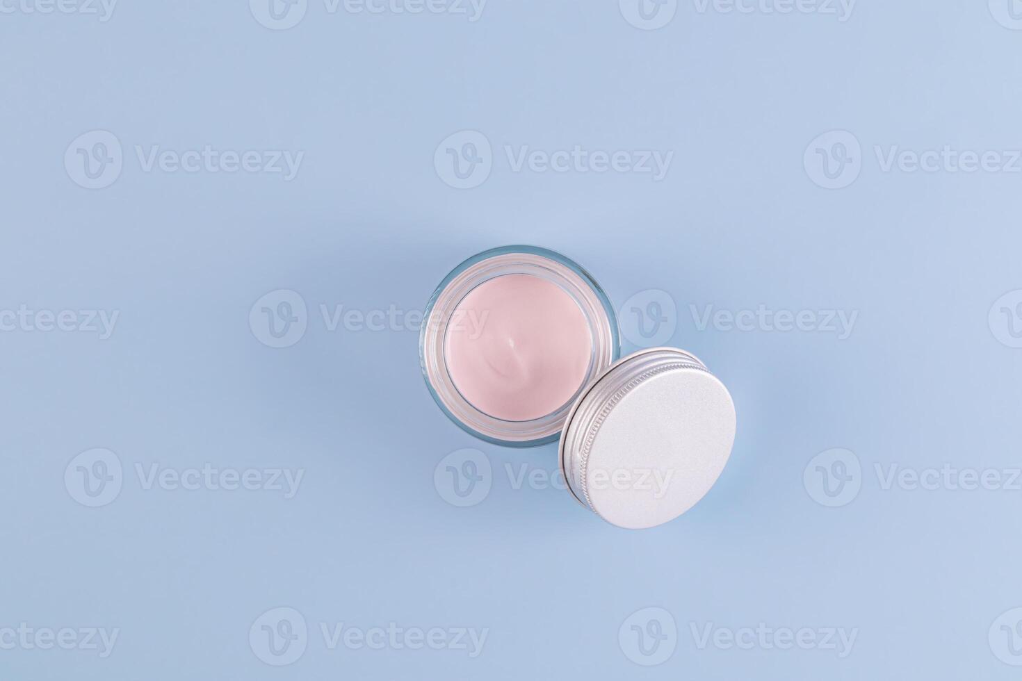 Open Glass Transparent Jar With Pink Cream For Young Skin Face And Body On Blue Background With Copy Space. Natural cosmetics. photo