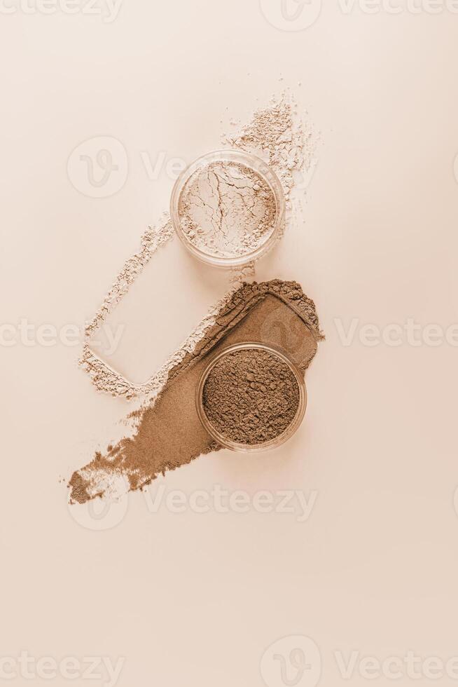 Two cosmetic jars with loose powder in natural and bronze tones on a beige background with powder strokes. Vertical top view. A copy space. Mockup. photo