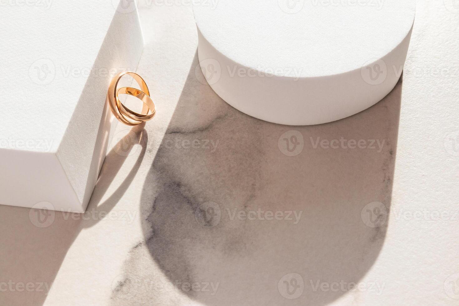 Two classic gold rings leaned on a white cube podium. Marble background. Sunlight. shadow of the figures. A copy of the space. Layout for design. photo