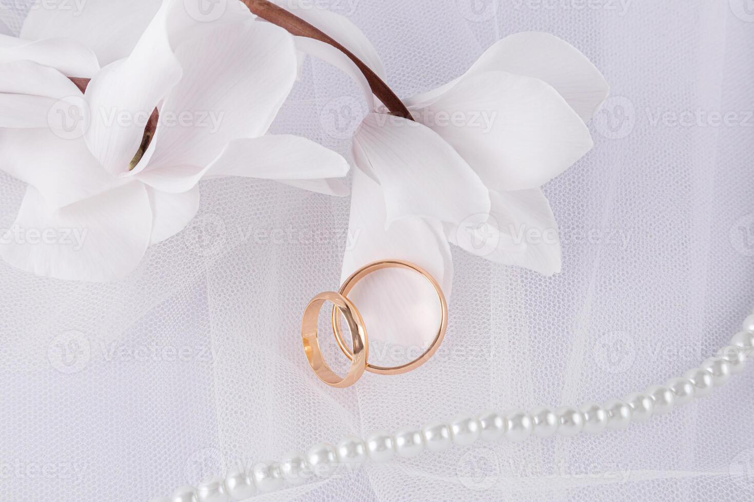 Beautiful wedding background in white color with delicate white flowers and gold wedding rings. Veil of the bride, pearl beads. Top view. photo