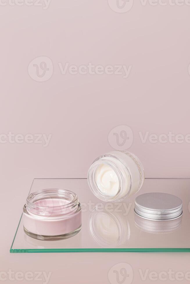 Pink and White Face and Body Skin Care Cream in Open Glass Cosmetic Jars on Glass Surface, Floating Shelf. Vertical view. A copy space. photo