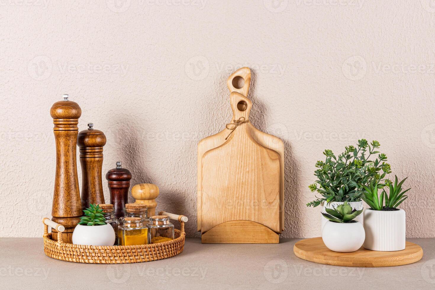 Set of wooden spice mills and glass jars with spices on a round wicker tray on a stone countertop in the interior of a modern kitchen space. photo