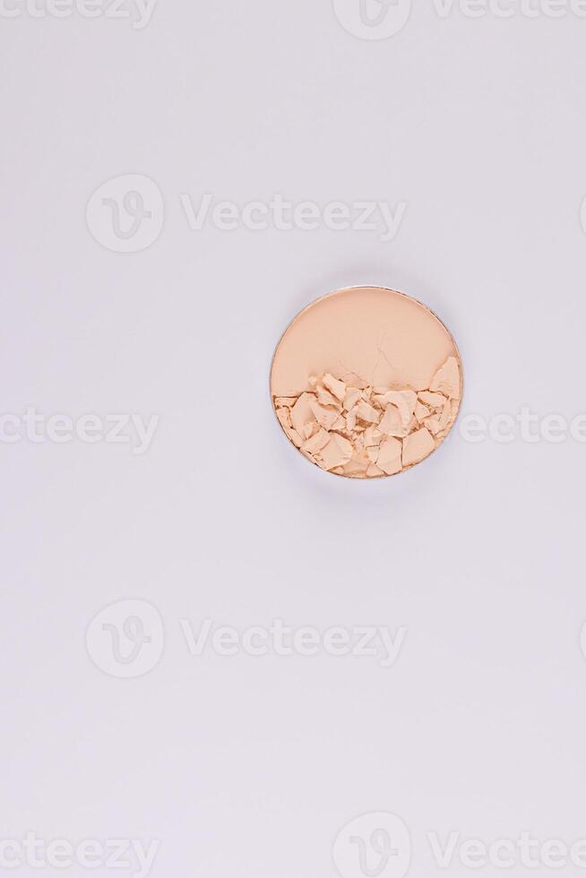 A compact powder in a natural beige color in a round block with broken pieces of texture. Top view. Vertical white background. layout. A copy space. photo