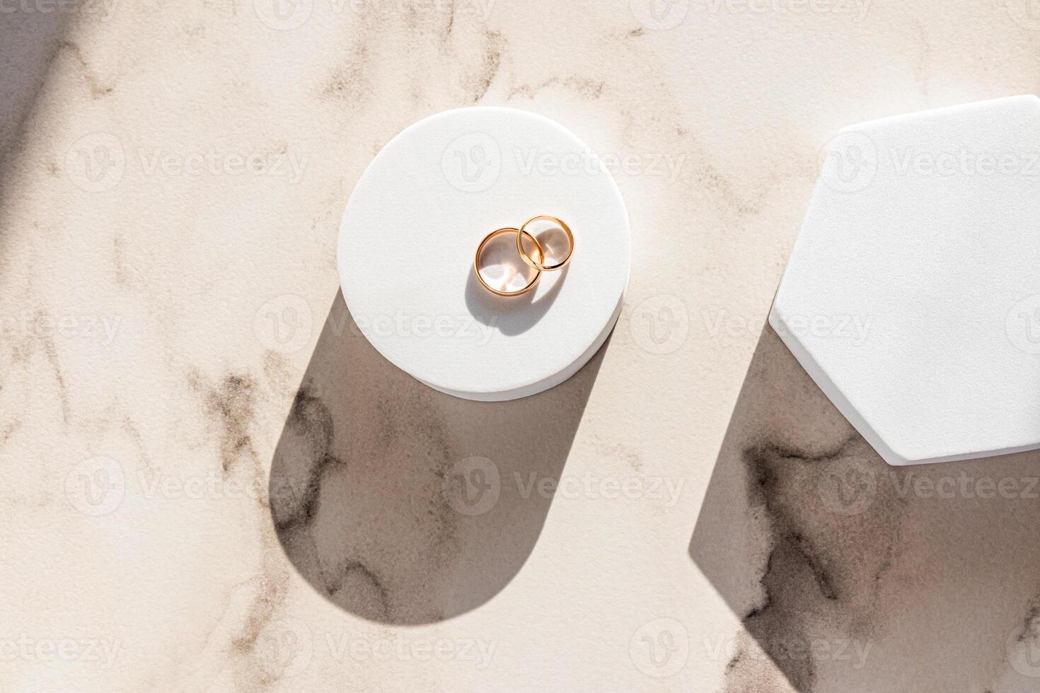 Two gold wedding classic rings lie on a white round podium on a marble background in the rays of the sun. Top view. A copy of the space. mockup. photo