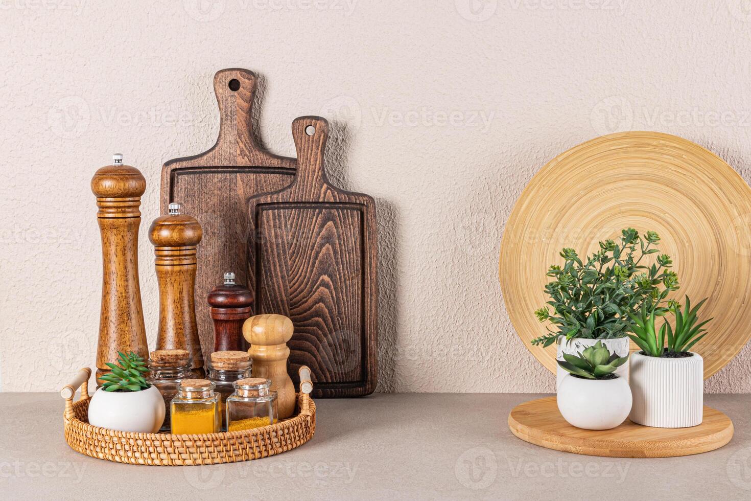 Set of wooden spice mills and glass jars with spices on a round wicker tray on a stone countertop in the interior of a modern kitchen space photo