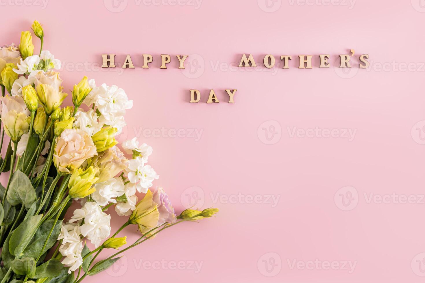 Beautiful bouquet in light colors of spring flowers on pink background with wooden letters and mother's day wish text. Holiday concept. photo