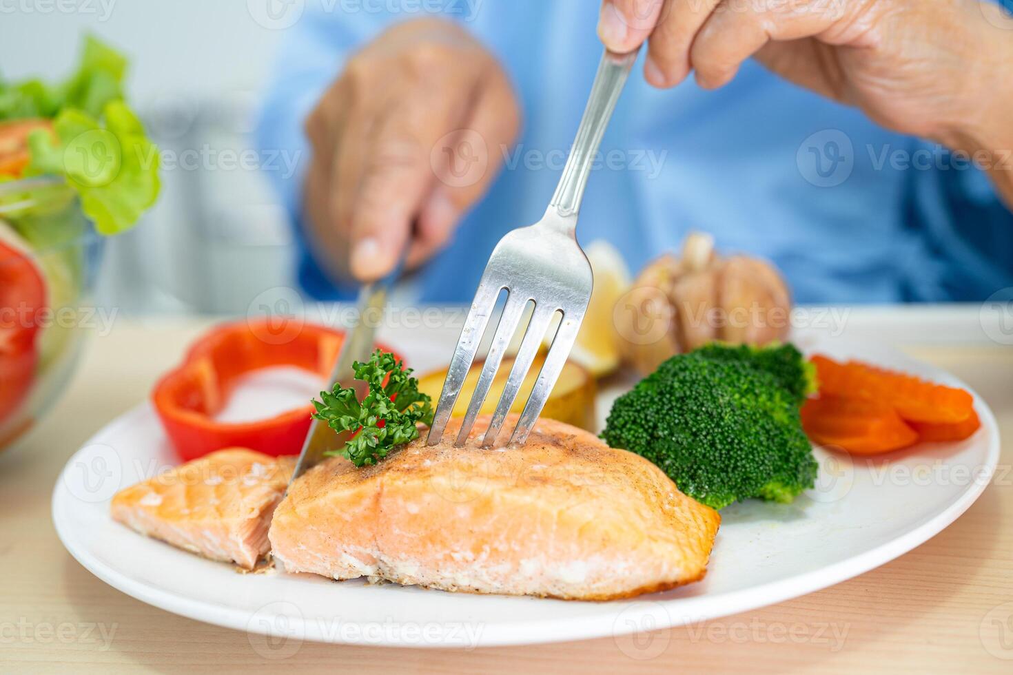 Asian senior woman patient eating Salmon steak breakfast with vegetable healthy food while sitting and hungry on bed in hospital. photo