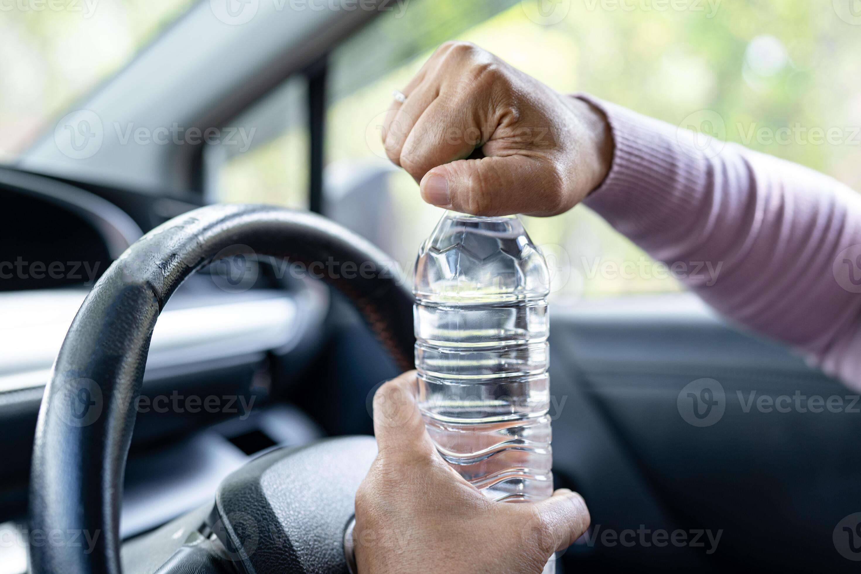 Asian woman driver holding bottle for drink water while driving a car. Plastic hot water bottle