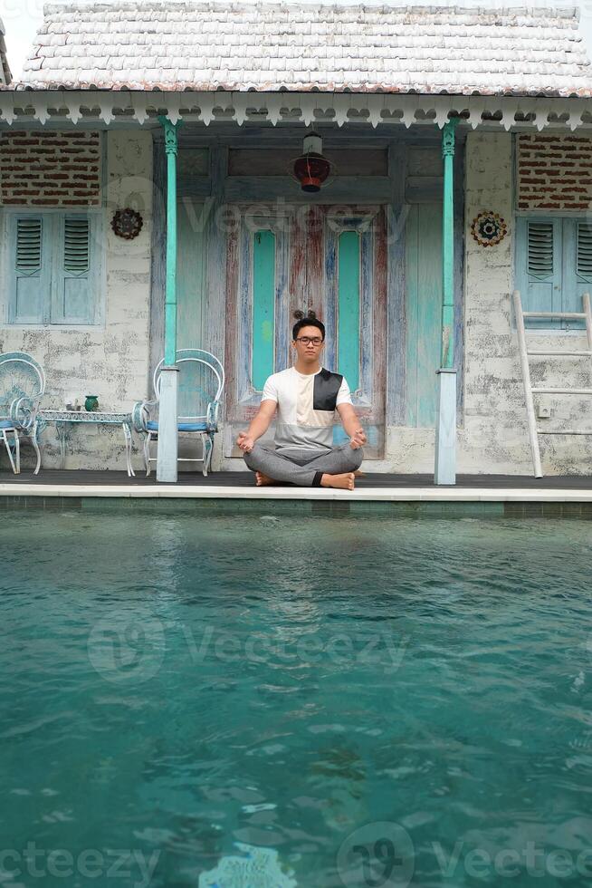 junto a la piscina serenidad, asiático modelo en loto yoga pose, bali villa relajación foto