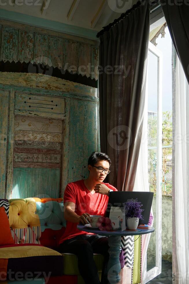 Asian Man Working on Laptop in Sunlit Villa, Sofa Comfort, Productivity photo