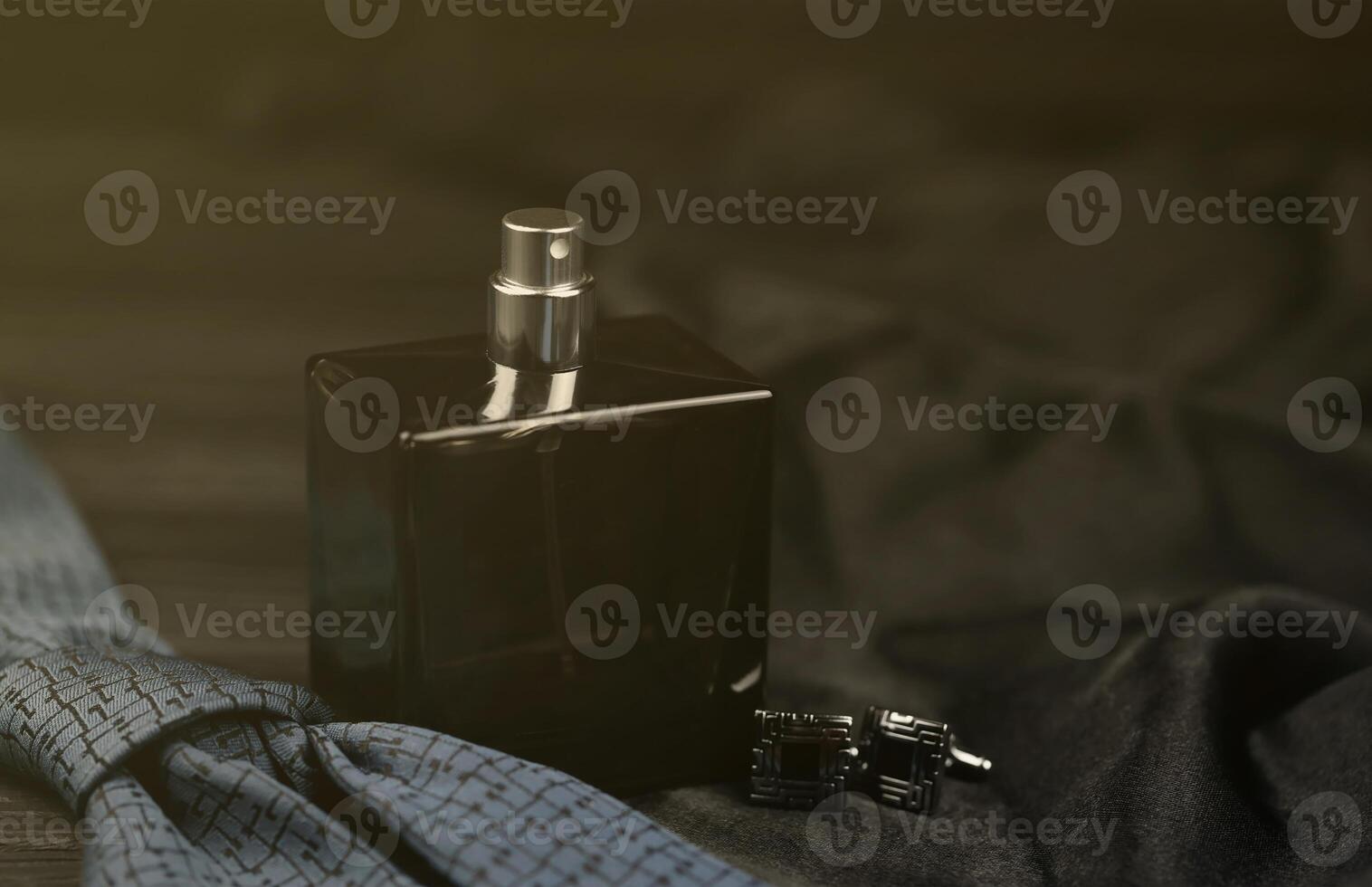 A bottle of mens cologne and cufflinks with blue tie lie on a black luxury fabric background on a wooden table. Mens accessories photo