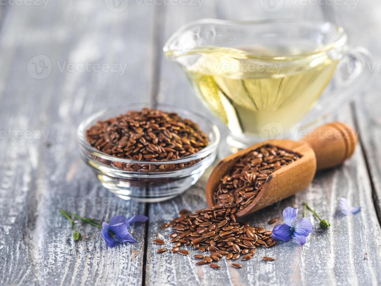 Flax seeds and flax oil. Brown linen seeds, flaxseed oil and blue flax flowers on old gray wooden background. Copy space photo