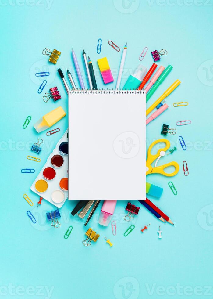 Online study, drawing, distantly painting class. Notebook, colorful stationery, supplies for drawing and craft. Empty notepad sketchbook sheet, shool supplies on blue. Vertical. Copy space, flatlay photo