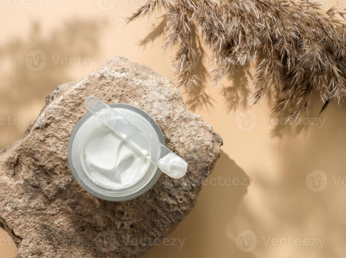 Cosmetic cream or moustirizer on stone, pampas grass on pastel beige background. Beautiful shadows. Open round glass jar with aesthetic swirls face cream and spatula. Flatlay. Copy space photo