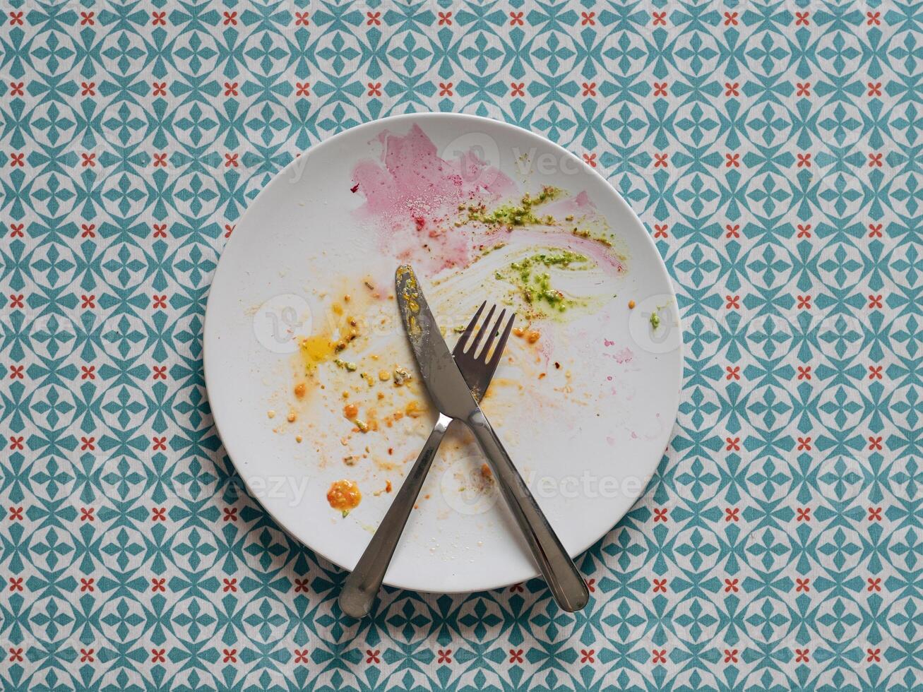 Dirty plate after healthy vegetarian paleo lunch. White plate and colorful dirty after egg yolk, beet and green pesto, over blue tablecloth. Top view or flat lay. photo