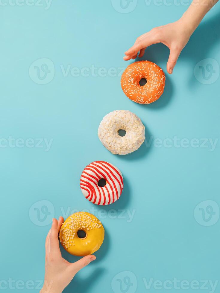 Two hands reach for donuts on blue background, top view. Creative layout with delicious glazed donuts. Vertical flat lay with diagonal made from donuts or doughnuts photo