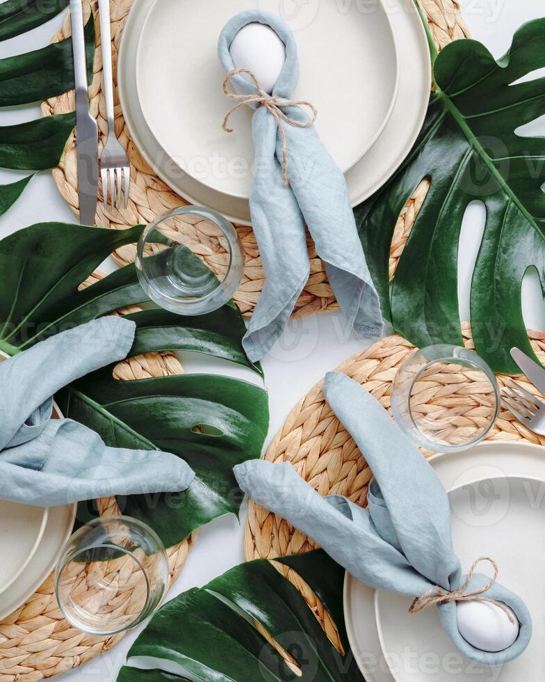 Tropical Easter Tablesetting. Top view of table setting for Christian Easter with bunny eggs decorated monstera leaves. Aesthetic Easter tablescapes. Easter dinner with bunny, tropical leaves and eggs photo