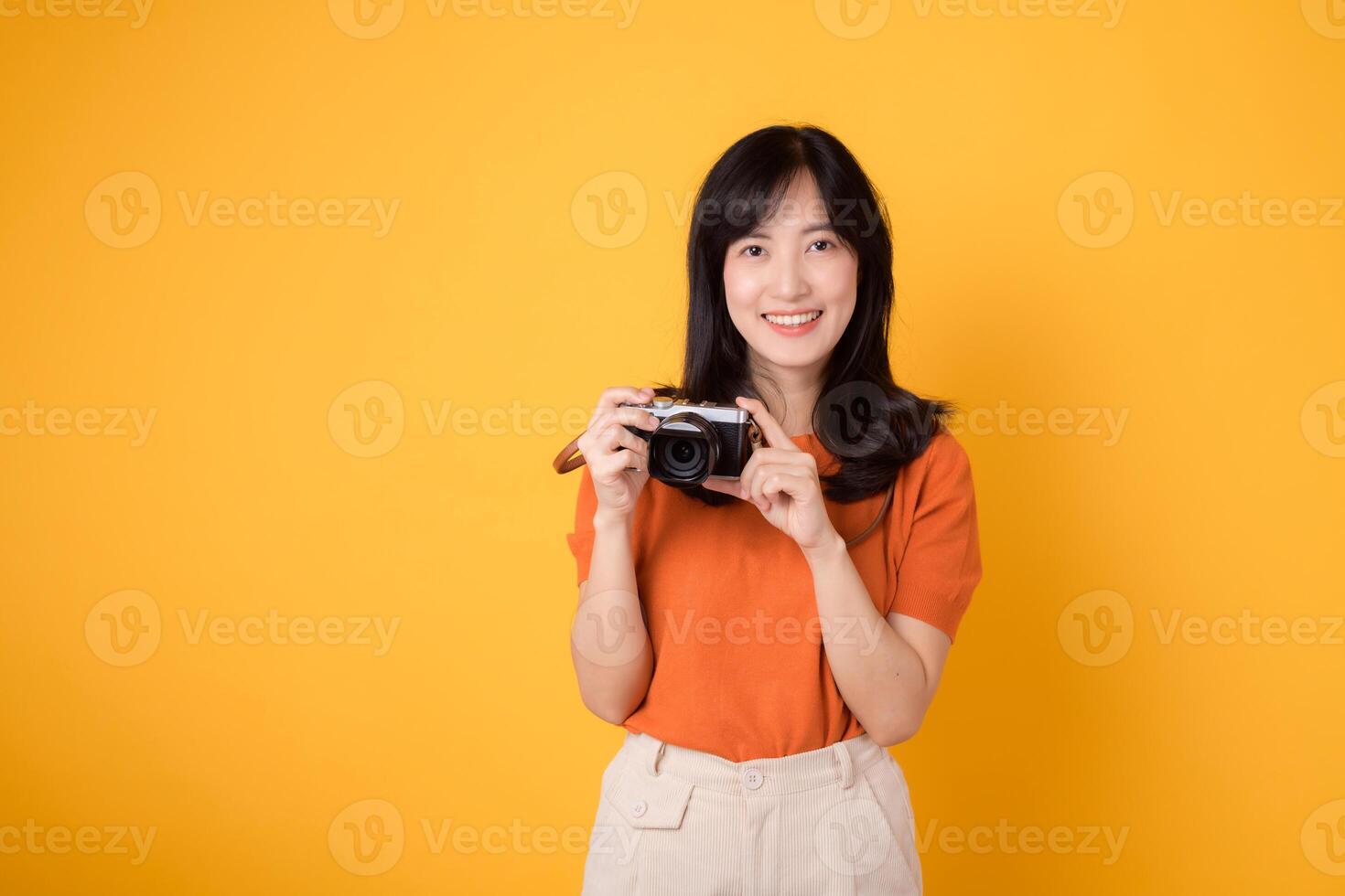 Young asian woman with a camera, ready for a fun adventure tour. Positive holiday vibes on a yellow background photo