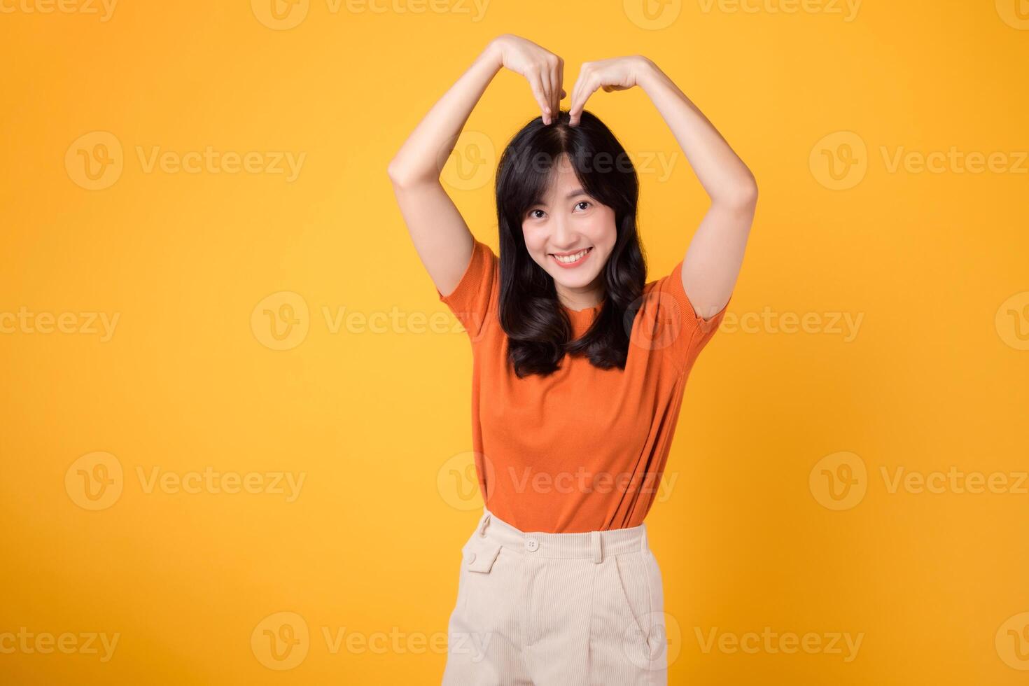 Expressive and genuine, a young Asian woman in her 30s showcases a heart gesture, embodying affection and joy, against a vibrant backdrop. photo