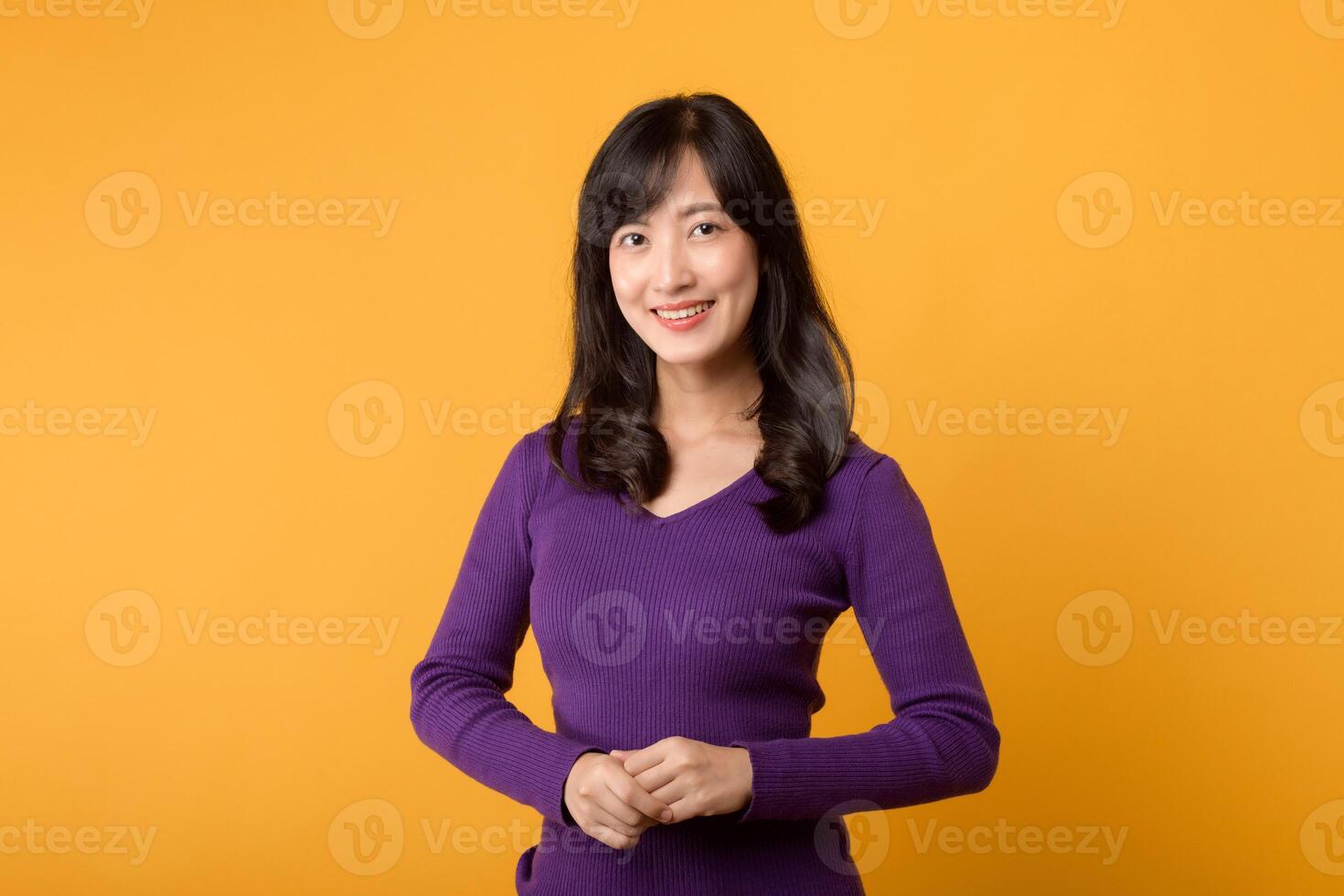 Young Asian woman in 30s wearing purple shirt, hands on hip isolate on vibrant yellow background. wellness life advertising concept. photo