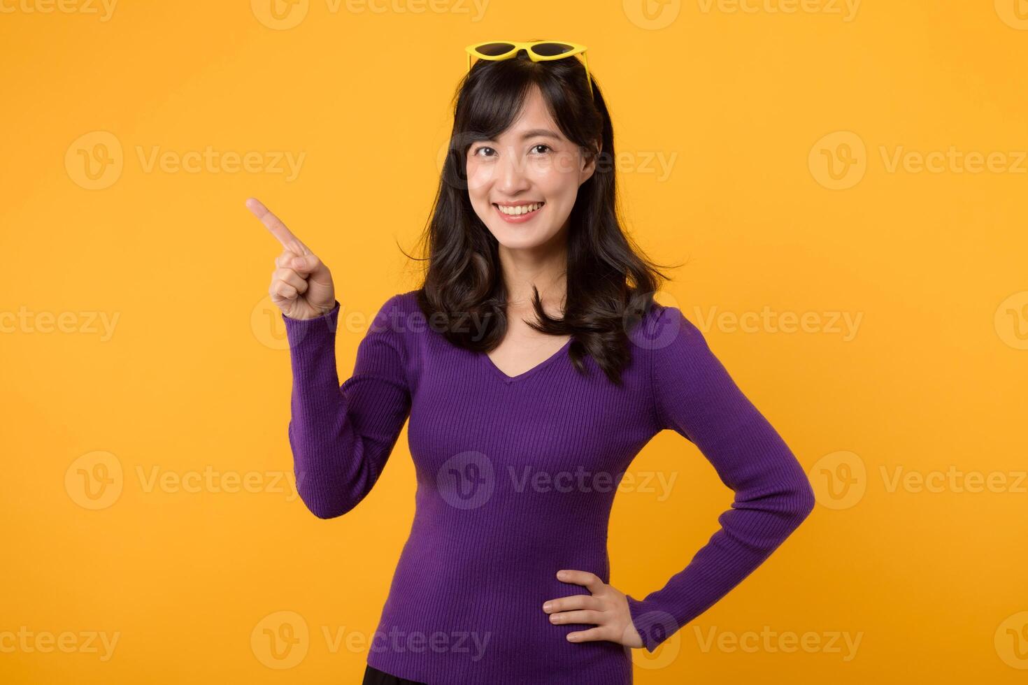 retrato alegre bonito joven asiático 30s mujer vistiendo púrpura suéter señalando dedo gesto a gratis Copiar espacio aislado en amarillo antecedentes. asiático bonito adulto demostración idea un gesto concepto. foto