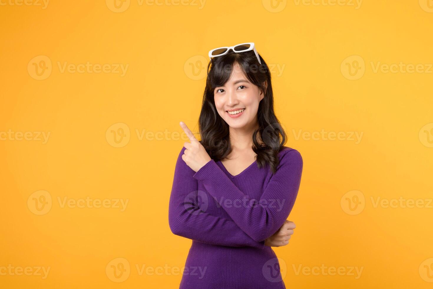 Beautiful young Asian woman 30s wearing purple shirt pointing up to copy space with smile face and happy. Pretty girl act like a satisfied product, use for advertising with yellow background photo