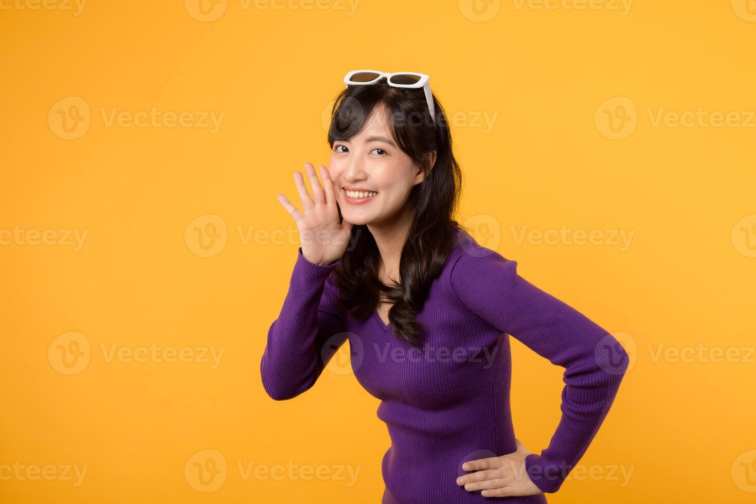 Portrait young beautiful 30s asian woman happy smile dressed in purple clothes shout to free space isolated on yellow studio background. Presenting product Beautiful girl act like telling to customer. photo