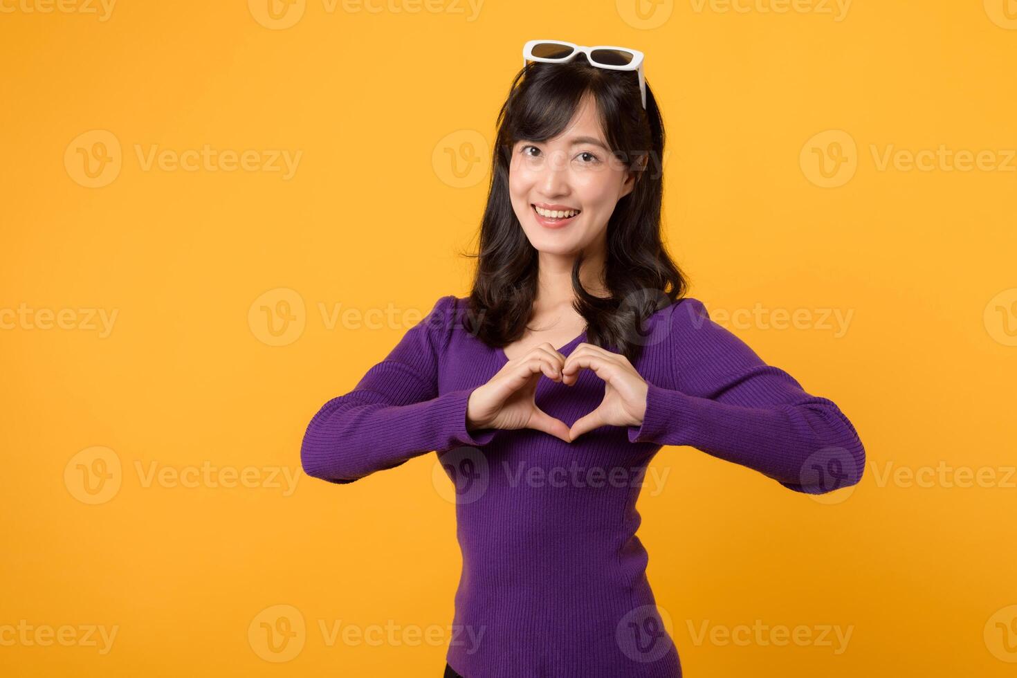 Expressing love and happiness on Valentine's Day, a cheerful young woman forms a heart shape with her hand in a studio portrait, symbolizing romance. photo