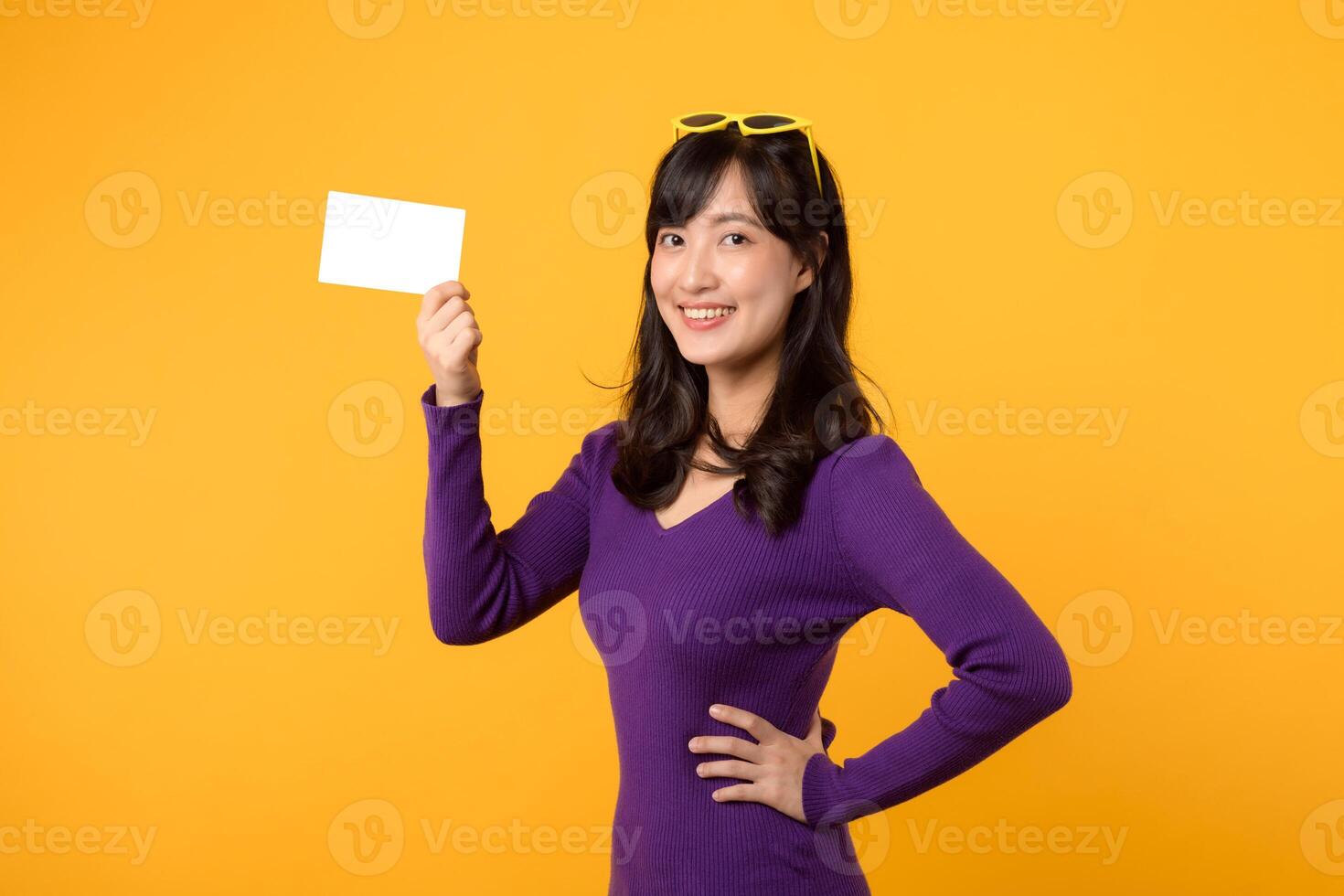 Against a vibrant yellow backdrop, a modern woman, in purple shirt and sunglasses, showcases an empty card, a blank slate for your message. photo