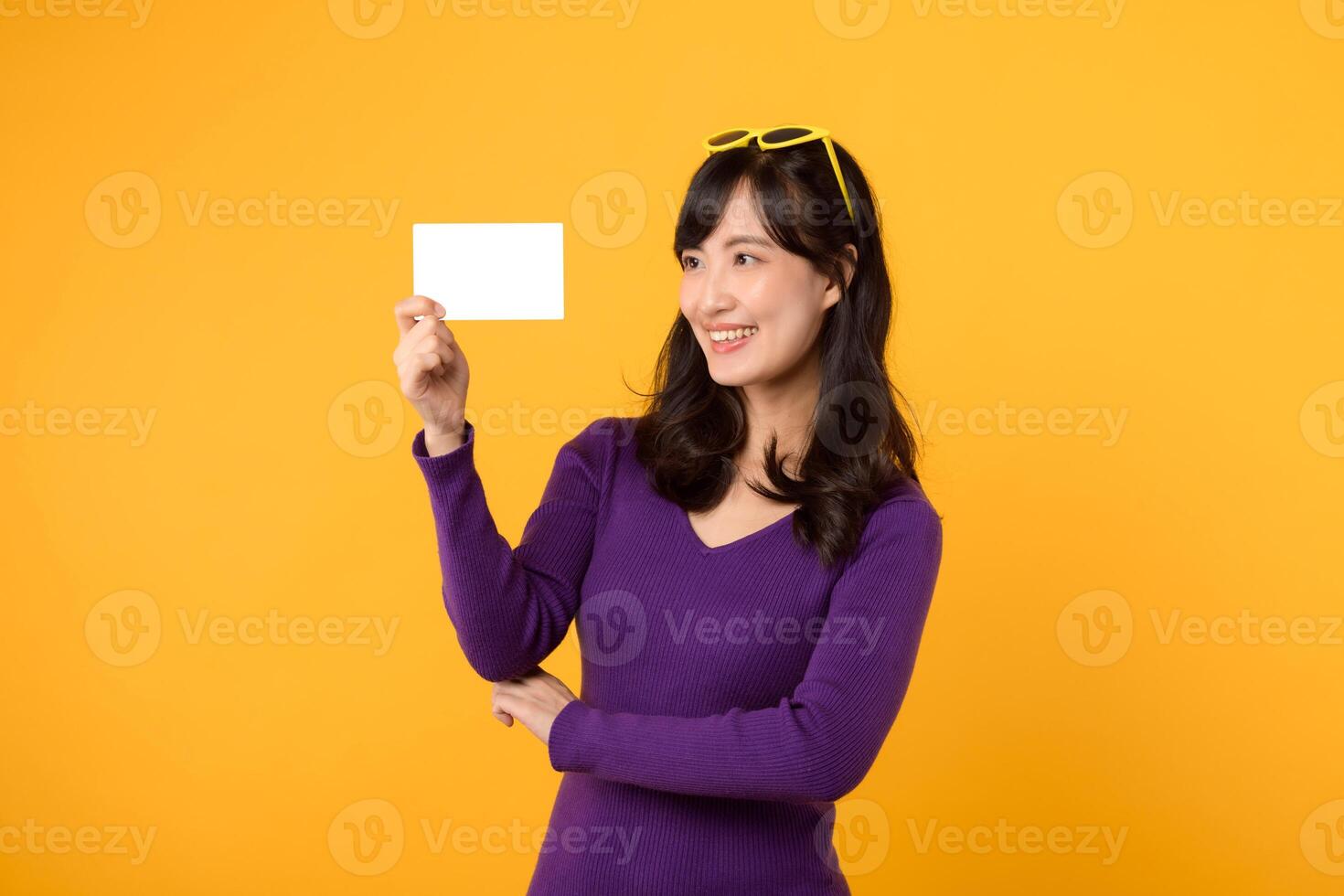 A modern woman, in purple shirt and sunglasses against a yellow background, holds an empty card, your opportunity for a compelling message. photo