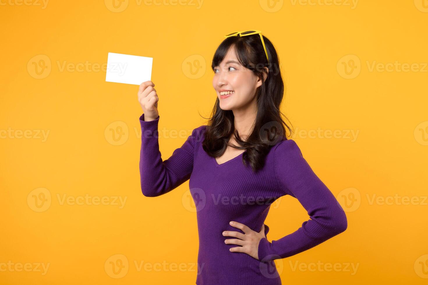 Beautiful pretty smiling asian woman 30s wearing purple shirt showing blank gift card isolated on yellow background. photo