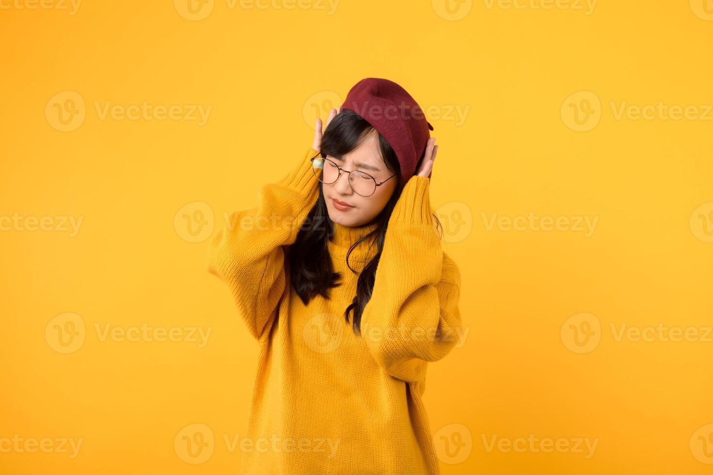 Noise stress getting to you. An upset lady, wearing a yellow sweater and red beret, seeks relief against a vibrant yellow backdrop. photo