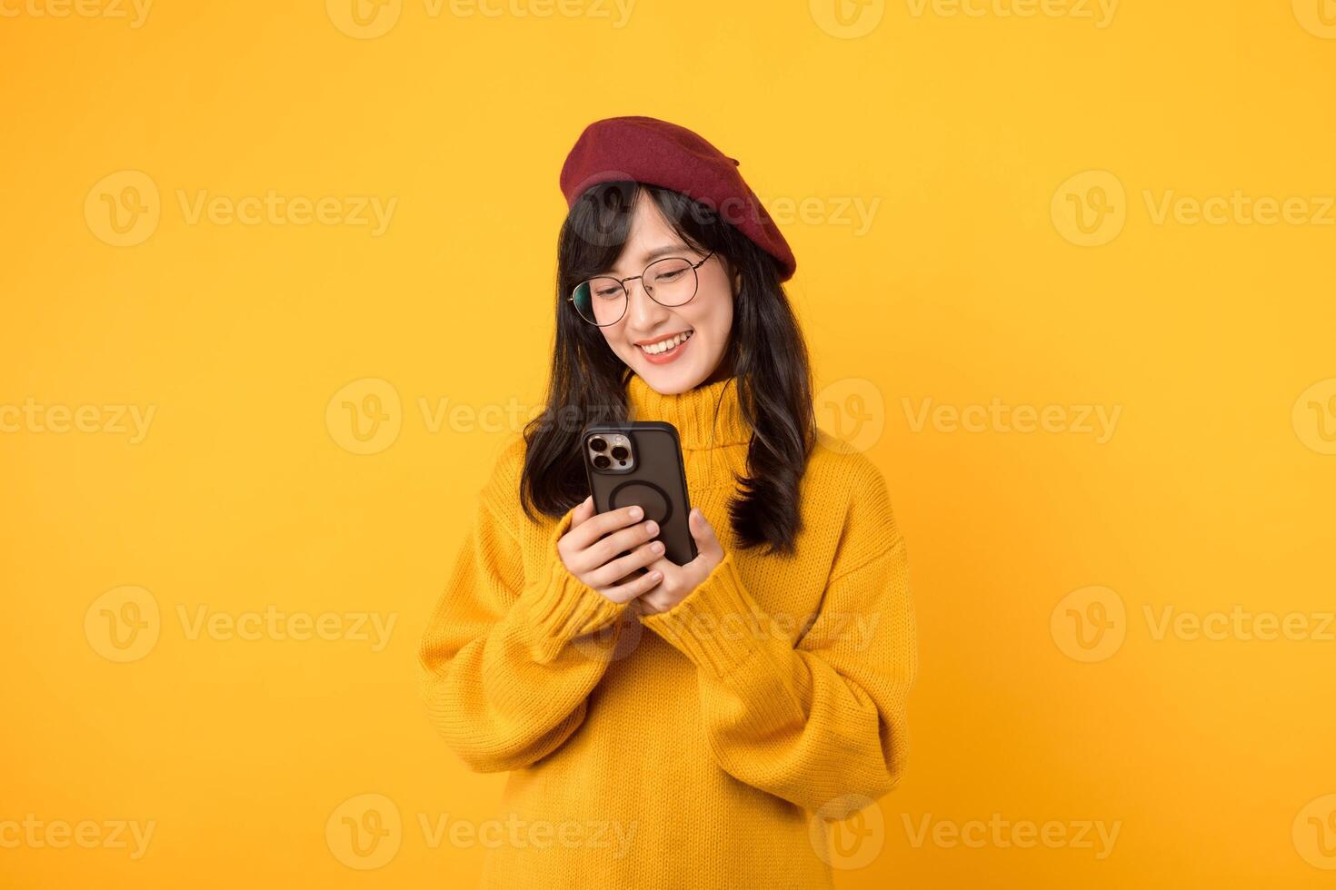 Portrait young pretty asian woman 30s wearing yellow sweater and red beret feeling happy while using smartphone explore the world. mobile application concept. photo