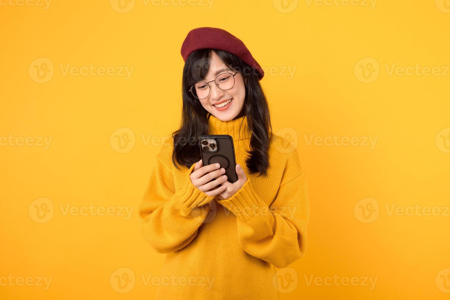 Portrait young pretty asian woman 30s wearing yellow sweater and red beret feeling happy while using smartphone explore the world. mobile application concept. photo