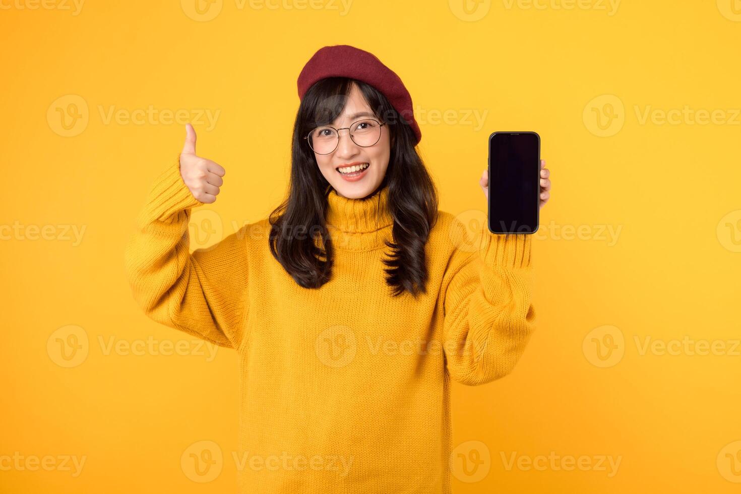 japonés, coreano, y chino etnias unido, demostración pulgares arriba mientras utilizando un teléfono inteligente en contra un vibrante amarillo fondo, vestido en rojo boina y los anteojos. foto