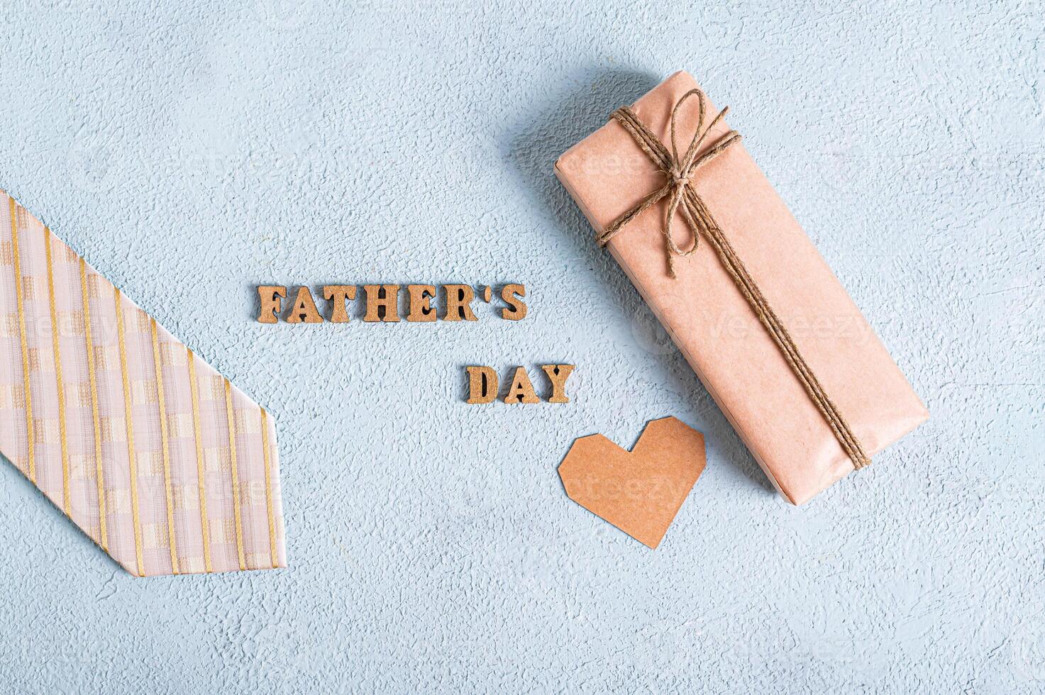 Father's day gift in craft paper, cardboard heart, tie and inscription on blue texture background photo