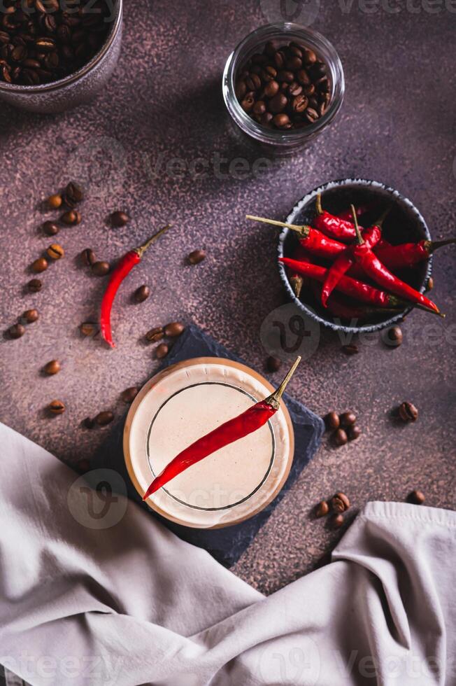 Cup of hot spicy coffee latte with red chili pepper on the table top and vertical view photo