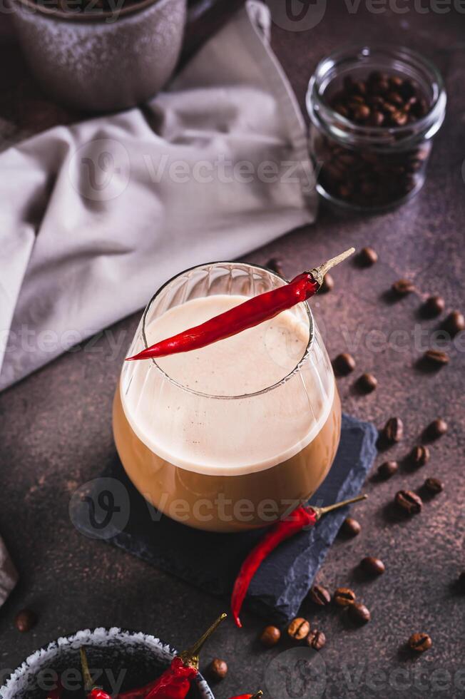 Cup of hot spicy coffee latte with red chili pepper on the table vertical view photo