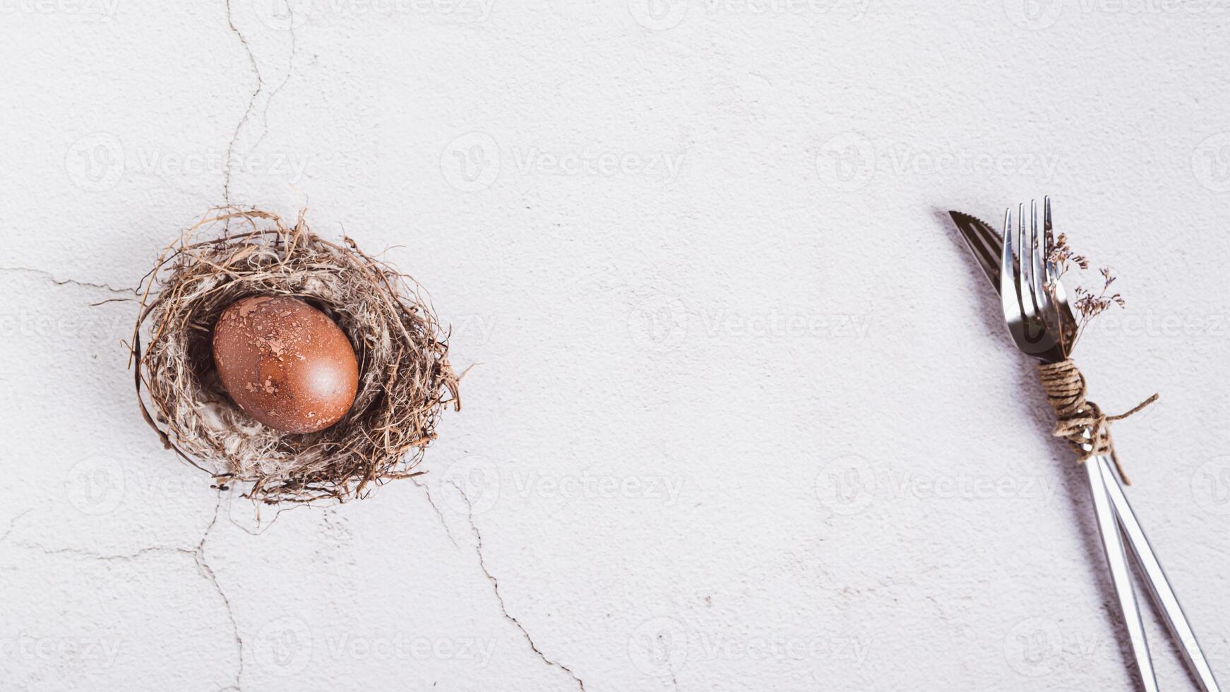 Homemade naturally colored egg in a nest and cutlery for Easter on the table top view web banner photo